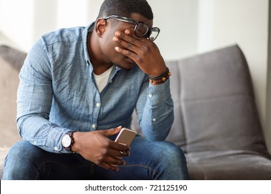 Feeling exhausted. Frustrated young black man massaging his nose and keeping eyes closed while sitting at his working place in office