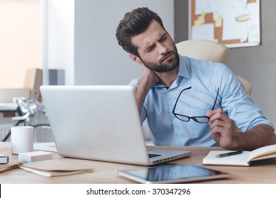 Feeling exhausted. Frustrated young handsome man looking exhausted while sitting at his working place and carrying his glasses in hand - Powered by Shutterstock