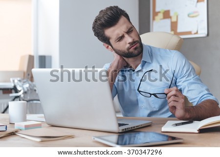 Feeling exhausted. Frustrated young handsome man looking exhausted while sitting at his working place and carrying his glasses in hand