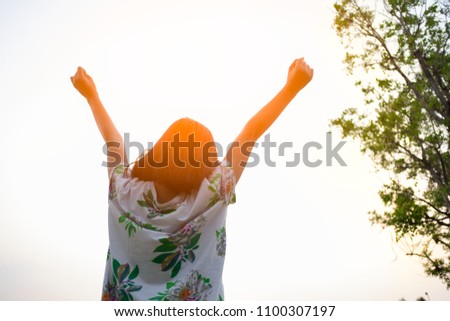 Feeling free. Upper body shooting from rear and low angle view of a young girl standing outdoor raising her arms up to sky to express good feeling. Image with copy space.