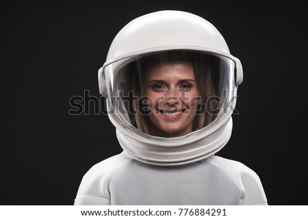 Feeling happiness. Portrait of charming delighted female astronaut wearing helmet and protective suit is standing and looking at camera with wide smile. Isolated background