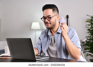 Feeling Happy And Confident. Young Asian Man Using Laptop Computer Holding Credit Card For Online Shopping And Payment At Home.