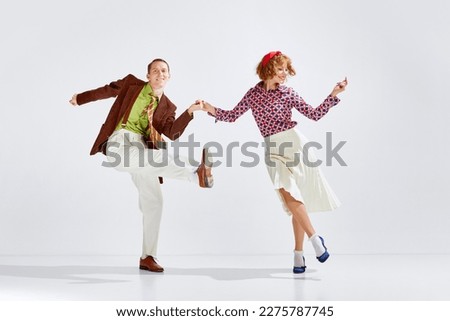 Feeling happy and positive. Young smiling man and woman in stylish clothes dancing retro dance against grey studio background. Concept of art, retro style, hobby, party, movements, 60s, 70s culture