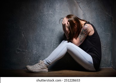 Feeling hopeless. Young woman trapped holding head in hands while sitting on the floor in a dark room