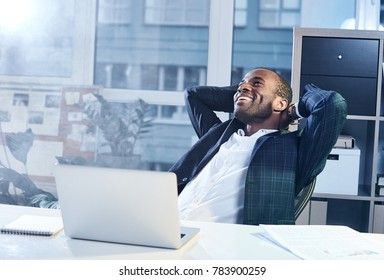 Feeling joy. Cheerful young elegant african businessman is reclining on chair and holding his hands behind head while looking up with wide smile