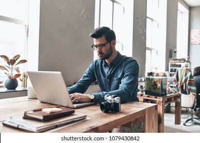 Feeling passionate about his project. Thoughtful young man using laptop while working in the creative working space - Shutterstock ID 1079430842