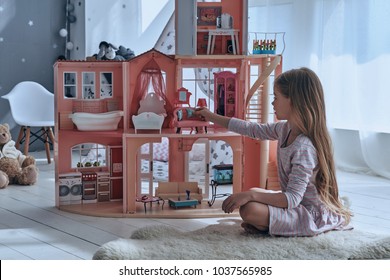 Feeling Playful. Cute Little Girl Playing With A Dollhouse While Sitting On The Floor In Bedroom