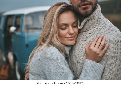 Feeling protected.  Beautiful young couple embracing and smiling while standing near the blue retro style mini van - Powered by Shutterstock