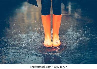 Feeling protected in her boots. Close-up of woman in orange rubber boots jumping on the puddle 