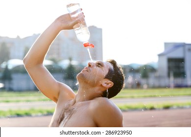 Feeling refreshment. Portrait of young man standing and pouring himself with water - Powered by Shutterstock