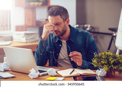 Feeling sick and tired. Frustrated young man massaging his nose and keeping eyes closed while sitting at his working place in office