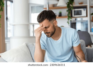 Feeling stressed. Frustrated handsome young man touching his head and keeping eyes closed while sitting on the couch at home