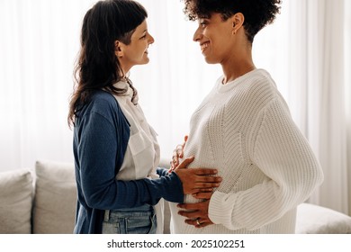 Feeling a surrogate mother's belly bump. Happy young woman smiling while feeling the movement of a pregnant woman's baby. Young woman spending time with her surrogate at home.