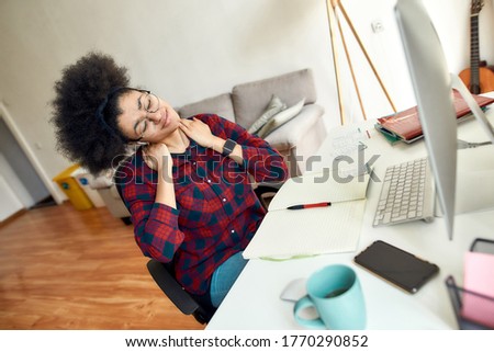 Feeling tired after studying online all day. Young afro american woman massaging neck and relaxing after long computer work at her workplace at home. Distance education. Stay home. Online school
