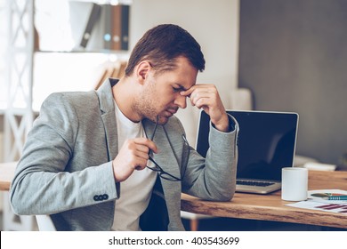 Feeling tired. Frustrated young handsome man looking exhausted while sitting at his working place and carrying his glasses in hand - Shutterstock ID 403543699