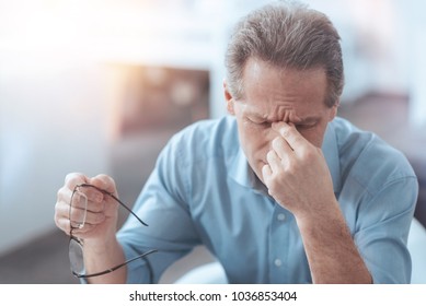 Feeling Tired. Nice Pleasant Senior Man Taking Off His Glasses And Holding The Bridge Of Nose While Being Tired From Work