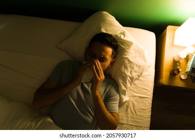 Feeling Very Sick. Hispanic Man With A Cold And Fever Blowing His Nose While Lying In Bed At Night 