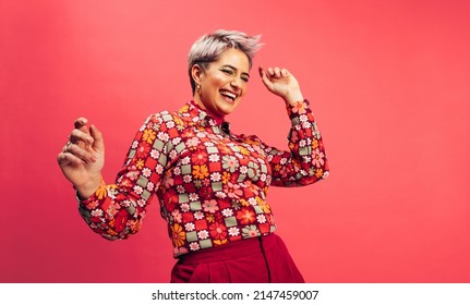 Feeling vibrant and energetic. Happy young woman dancing and smiling cheerfully while standing against a red background. Young woman with dyed hair having fun in the studio. - Shutterstock ID 2147459007
