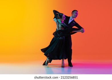 Feelings  Dynamic portrait young beautiful man   woman dancing ballroom dance isolated over gradient orange pink background in neon light  Concept art  beauty  grace  action  emotions 