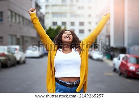 Feels great to be young and alive. Cropped shot of a happy young woman celebrating with arms raised against a city background.