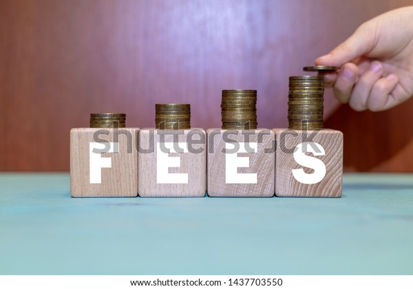 Fees Hidden Service Business concept. Hand puts\
coin on growing coins pyramid on wooden blocks with fees word.\
Cost, fee and taxes.