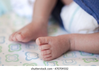 Feet Of A 2-week-old Baby Wearing Diapers Lying On The Bed At Home.