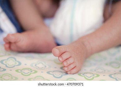 Feet Of A 2-week-old Baby Wearing Diapers Lying On The Bed At Home.