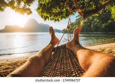 Feet Of Adult Man Relaxing In A Hammock On The Beach During Summer Holiday