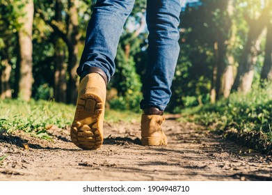 Feet Of An Adult Wearing Boots To Travel Walking In A Green Forest. Travel And Hiking Concept.