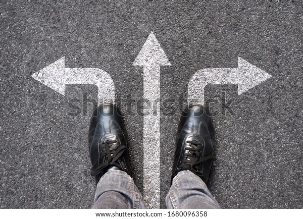 Feet and arrows on road background. Selfie feet\
above. Businessman standing on pathway with three direction arrows\
choice or move forward. Top view of business shoes walking.\
Motivation and growth.