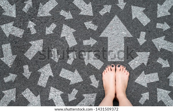 Feet and Arrows on Road. White Arrow Choice\
Concept. Woman Bare Feet with Gray Nail Polish Manicure Standing on\
Grunge Concrete with Many Arrow Sign Choices. Future Life with Many\
Direction Sign.