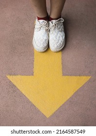 Feet And Arrows On Road. Yellow Straight Arrow Sign And White Shoes. Straight Direction Concept. Journey Concept

