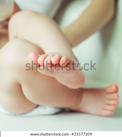 feet of a baby,  in bed at home with his mother on the background