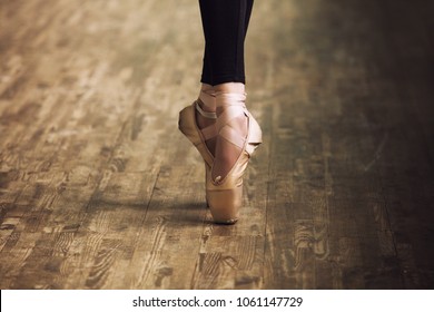 Feet of ballerina in training shoes on the parquet wooden floor close up retro style