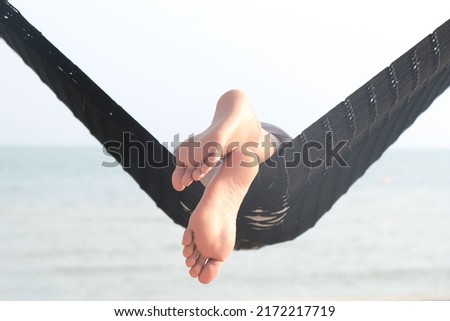 Feet of a beautiful woman. She lies in a hammock on the beach of the sea. In the summer she feels the good weather. she is on vacation