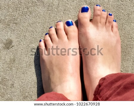 Feet with blue nail polish side by side on pavement.