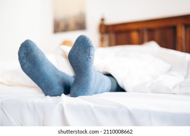 Feet With Blue Socks Sticking Out From Under The Duvet In Bed