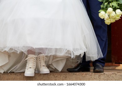 Feet Of The Bride And Groom Outdoors. A Girl In White Shoes And A Man In Black Shoes Before The Wedding Ceremony Outside In A Cold Day