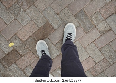 Feet in casual sneakers standing on a textured brick pavement, emphasizing urban simplicity and everyday perspective. - Powered by Shutterstock