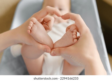 Feet of a child in mother's hands in the shape of a heart, close-up.Maternal love for her baby. Maternity leave, motherhood, happy childhood concept