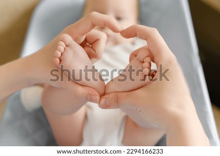 Feet of a child in mother's hands in the shape of a heart, close-up.Maternal love for her baby. Maternity leave, motherhood, happy childhood concept