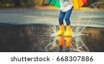Feet of child in yellow rubber boots jumping over a puddle in the rain
