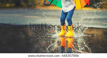 Feet of child in yellow rubber boots jumping over a puddle in the rain