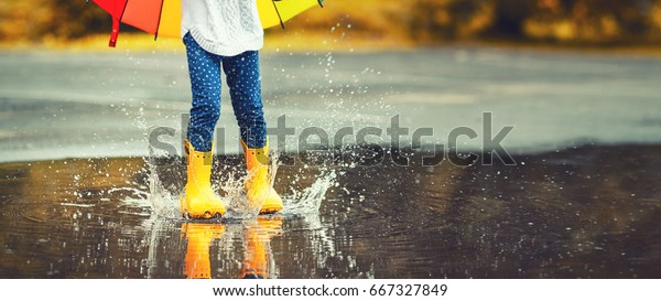 黄色いゴムのブーツをはいた子供の足が雨の中水たまりの上を跳び越えている の写真素材 今すぐ編集