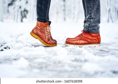 Feet of a couple on a snowy sidewalk in brown boots. Girl stands on toes while kissing. Winter weather concept