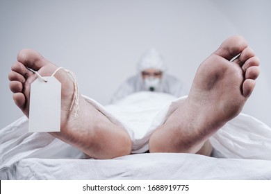 Feet Of A Dead Body, With An Identification Tag - Blank Sign Attached To A Big Toe. Covered With A White Sheet. Coronavirus Victim.