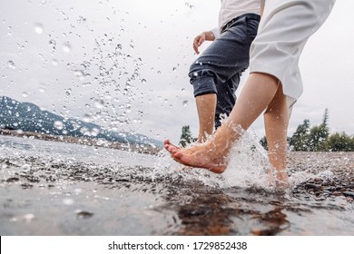 Feet exploding water. Legs at shore. Two people walking with naked legs on river shore. Pebbles under bare foot. Summer river.