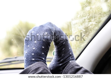 Feet in funny socks near the windshield of the car in a day and blurred landscape background