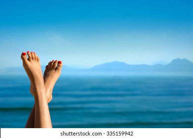 Feet of girl on the background of mountains. Girl at the resort. Female feet on sea background. Girl sunbathes on a beach. Meditation on the sea. Red pedicure.