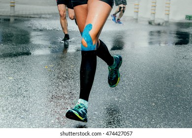 feet girl runners in compression socks and taping on his knees, running on wet asphalt - Powered by Shutterstock